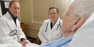 two doctors speaking with an elderly white woman in a hospital bed